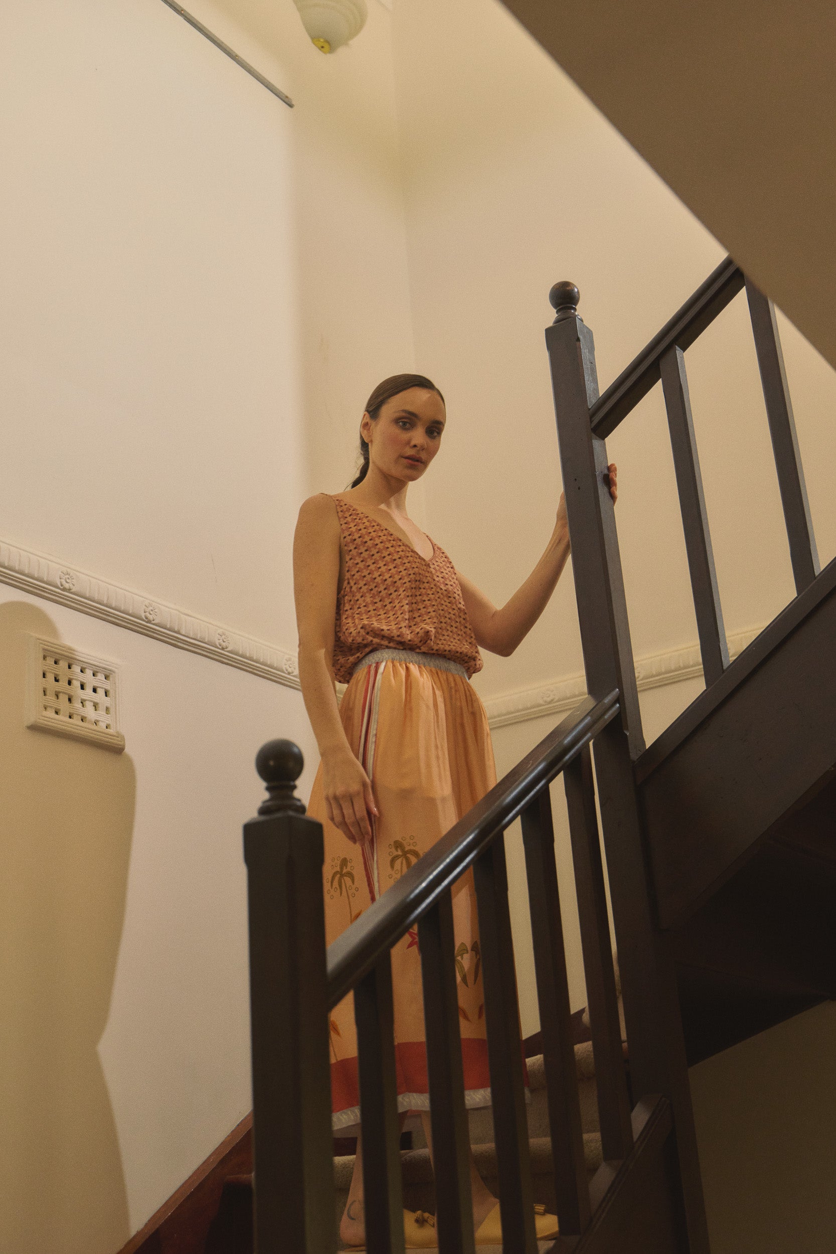Woman standing on a staircase wearing a peach patterned tank top and skirt.