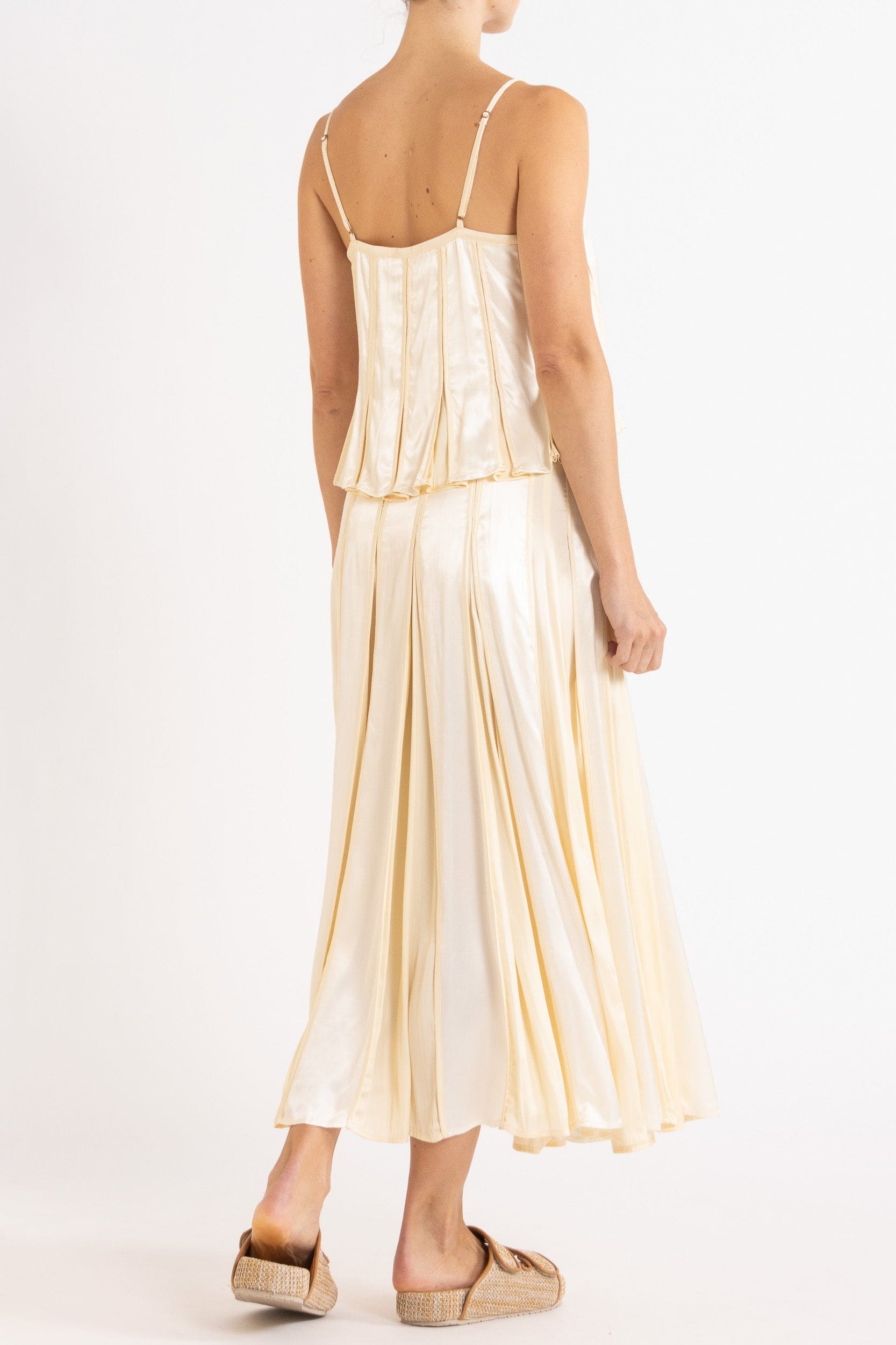 Model wearing cream box pleat camisole & skirt, side-back view