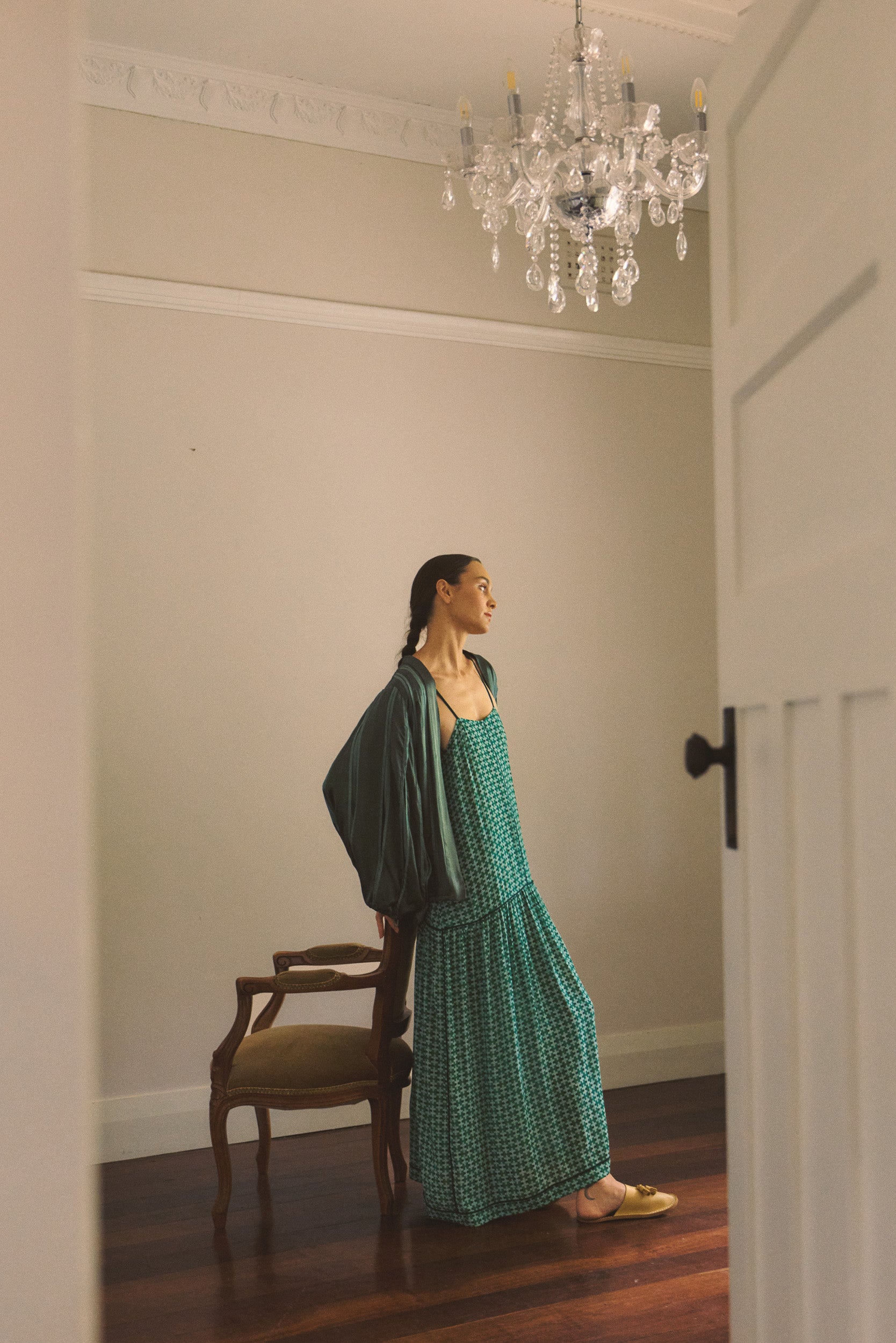 Woman in a green dress and jacket standing in a room with a chandelier.
