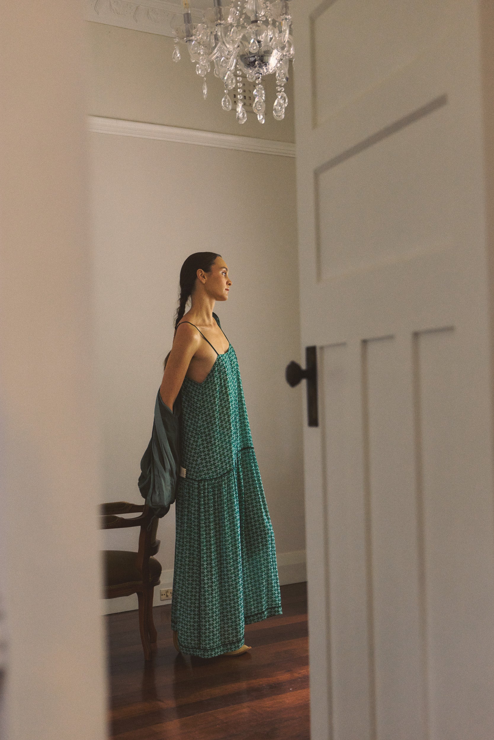 Woman in a green dress and jacket standing in a room with a chandelier.