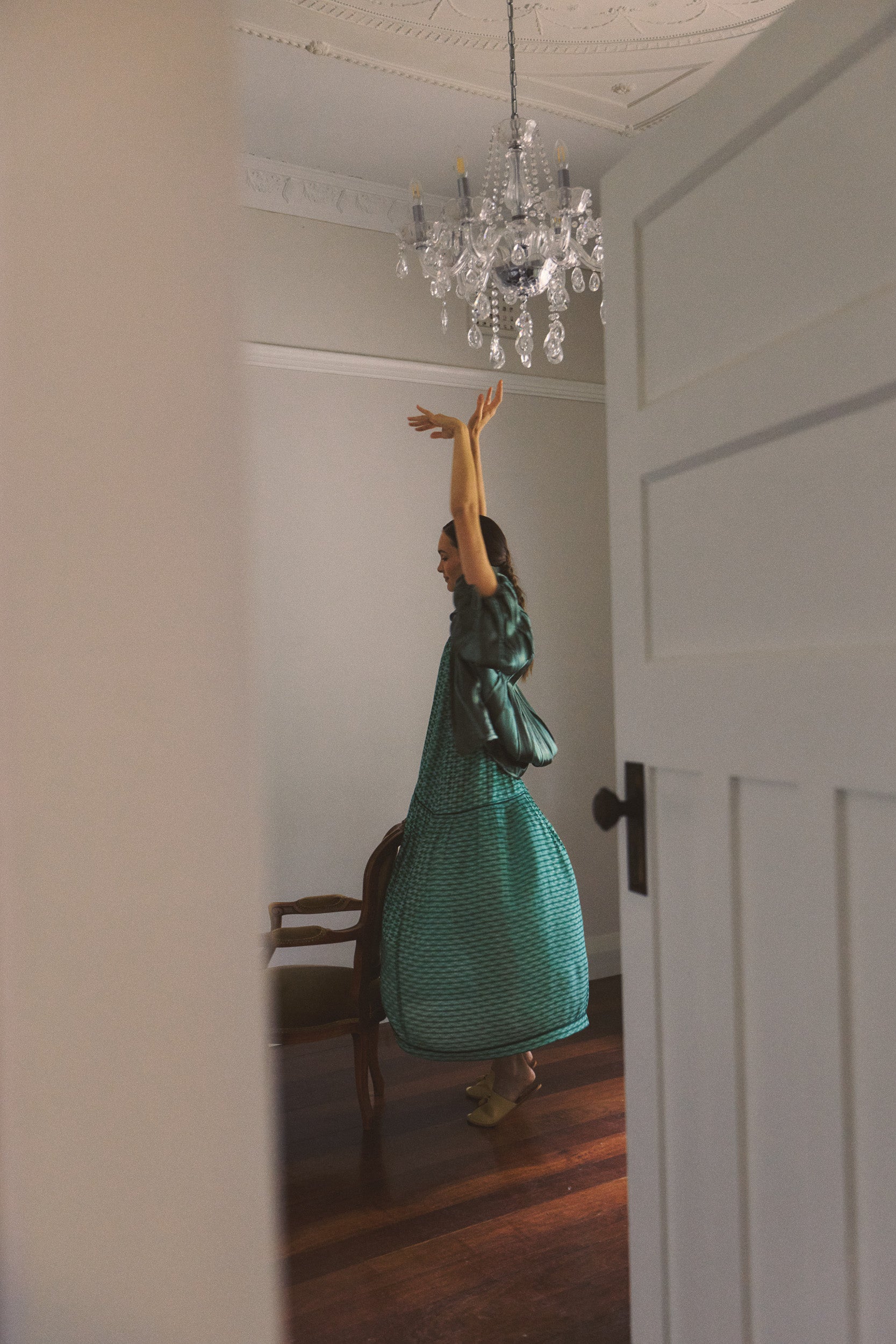 Woman in a green dress and jacket standing in a room with a chandelier.